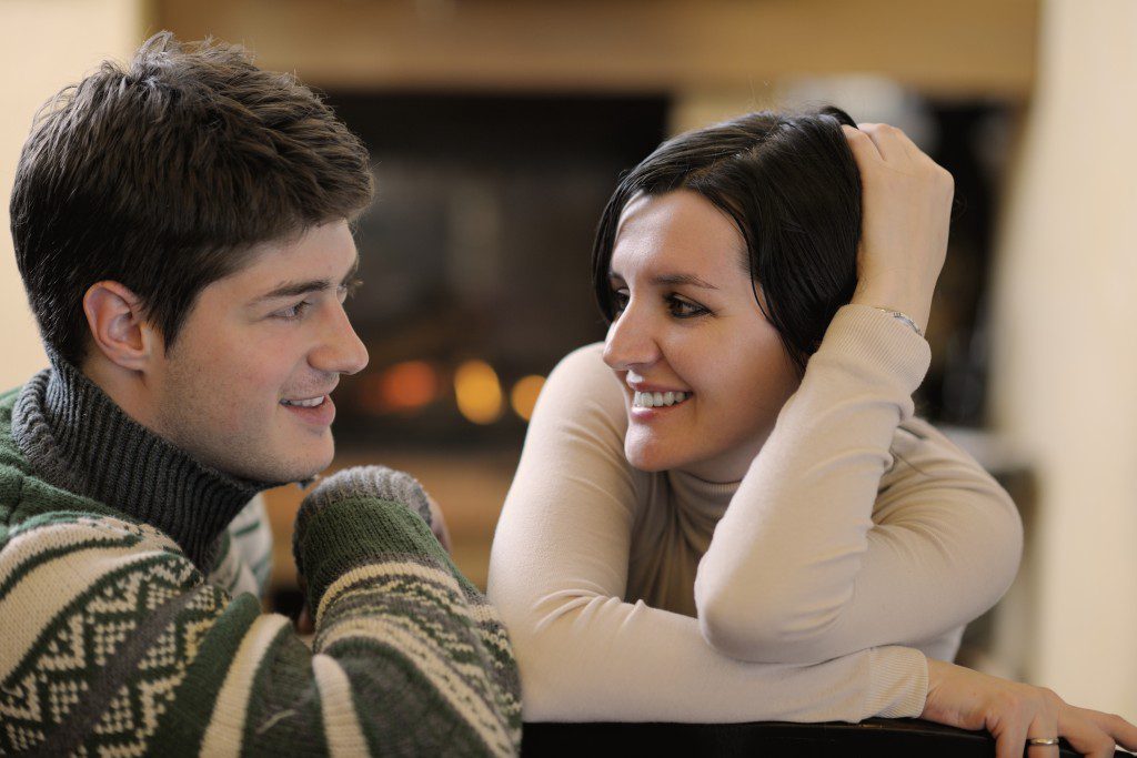 Young romantic couple sitting on sofa in front of fireplace at h